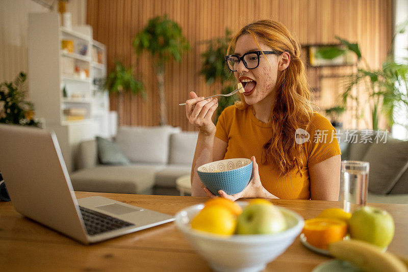 年轻女子早餐吃水果，用笔记本电脑