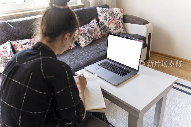 女孩用笔记本电脑学习。女孩在听在线教育课程。白皮肤的女孩在做笔记。