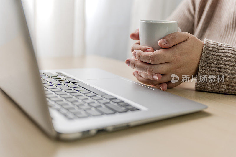 在家靠窗办公的女人拿着笔记本电脑和智能手机，喝着咖啡