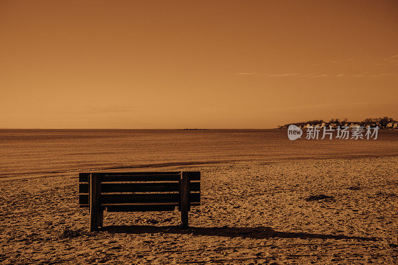 戏剧性的火热单色荒凉的海滩场景与空长凳和脚印