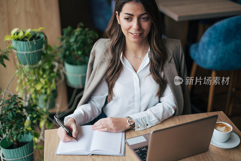 一个漂亮的女商人拿着笔记本电脑和一杯咖啡坐在咖啡馆里