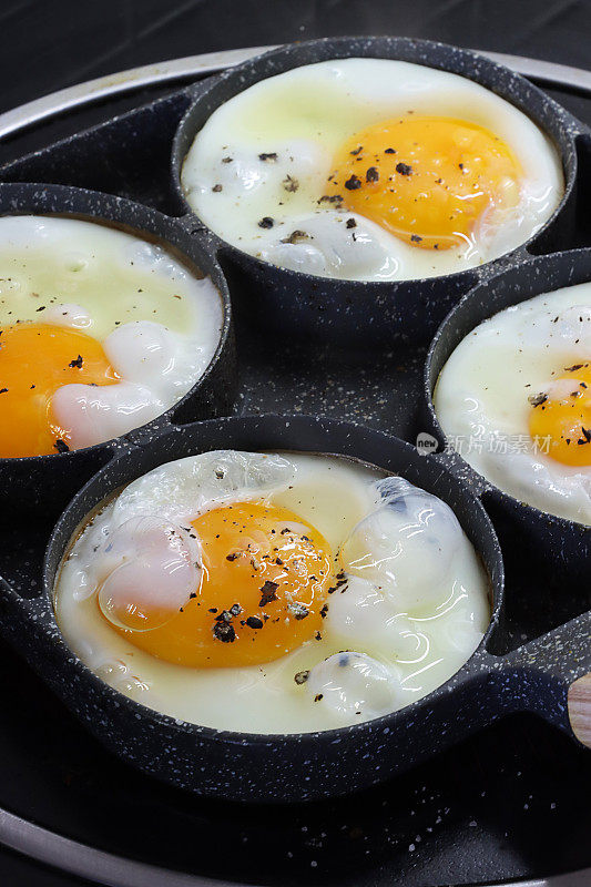 不粘锅的特写图像，有煎鸡蛋的环，四个鸡蛋在陶瓷滚刀上的煎锅里煮，升高的视图，重点在前景