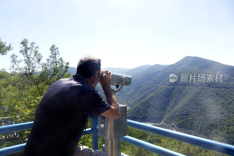 中年男子用投币操作的双筒望远镜看风景