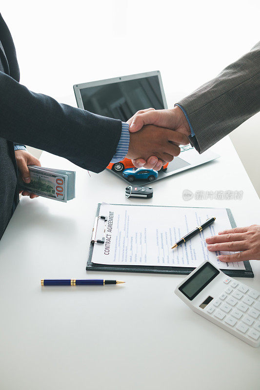 客户与汽车经销商在签订销售合同后握手，然后支付合同款项并将车钥匙交给客户。客户和汽车经销商之间握手的概念。