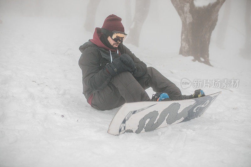男子从滑雪板上摔下来后坐在雪地上