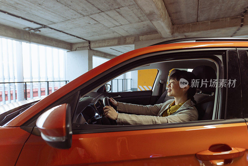 一个微笑的亚洲城市女人坐在车里，双手放在方向盘上