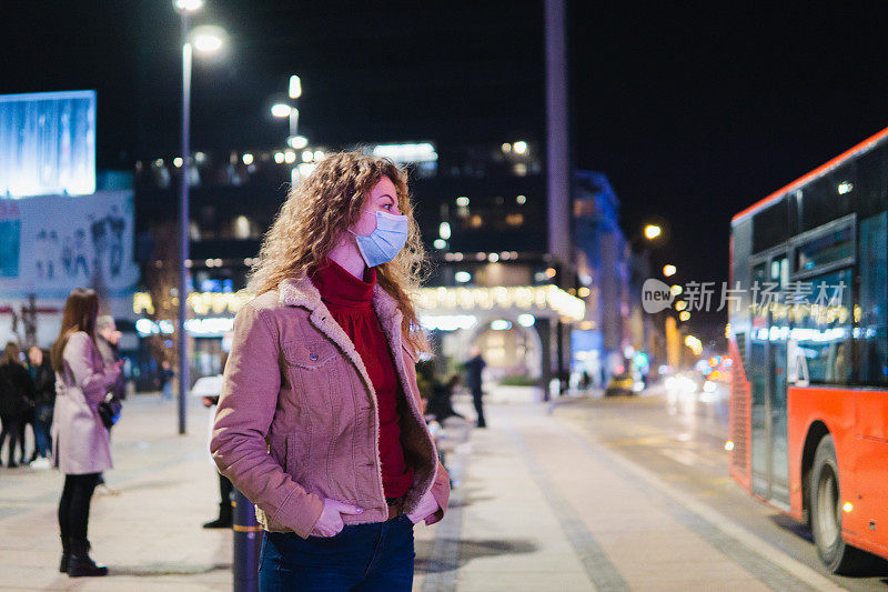 一个戴着口罩在晚上等公交车的女人