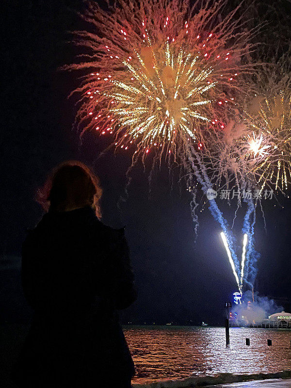 特写图像的年轻女子剪影在海滩上站在水边观看烟花表演，烟雾和火花在夜空