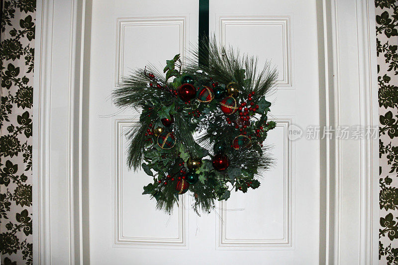 圣诞节花环由美丽的红、绿、金小饰品和松枝制成，挂在英国居民区的门上，这是圣诞节的传统