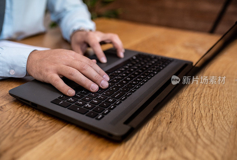 特写镜头。手和笔记本电脑。一个年轻的白领正坐在他的办公室里，在他的笔记本电脑上打字。