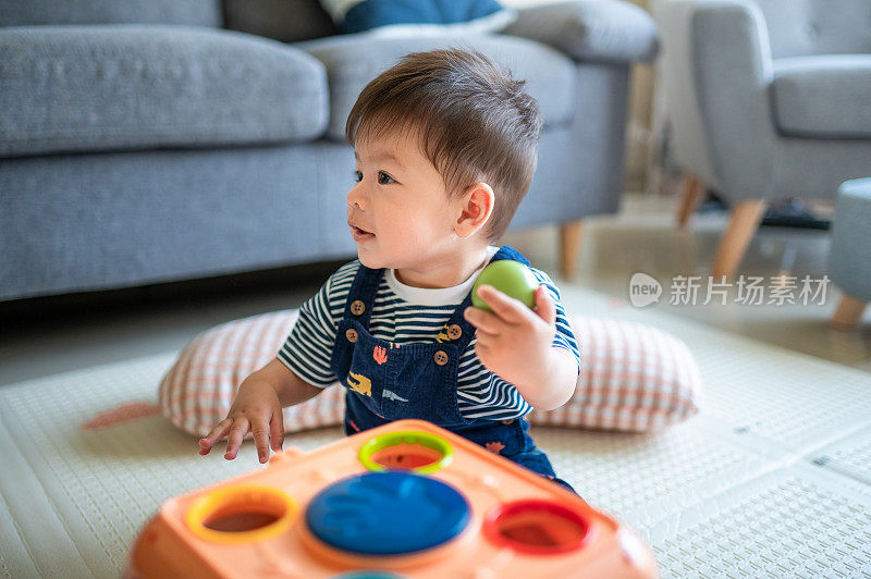 小男孩坐在地板上玩小球，把它们放在客厅的活动箱里