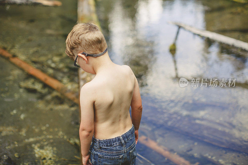 小男孩在森林溪流上的原木上保持平衡