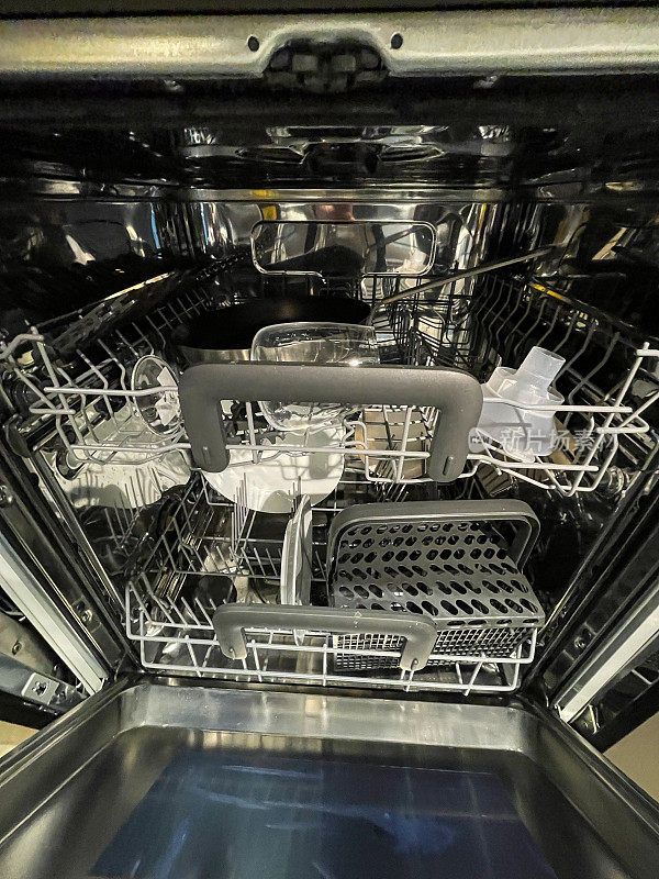 洗碗机内部的图像，空的塑料餐具篮，半满的机器，干净的煎锅和待清洗和干燥后收纳的酒杯