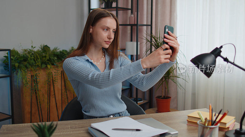 年轻的女博主在家里工作的时候用智能手机拍自拍照用于社交媒体vlog