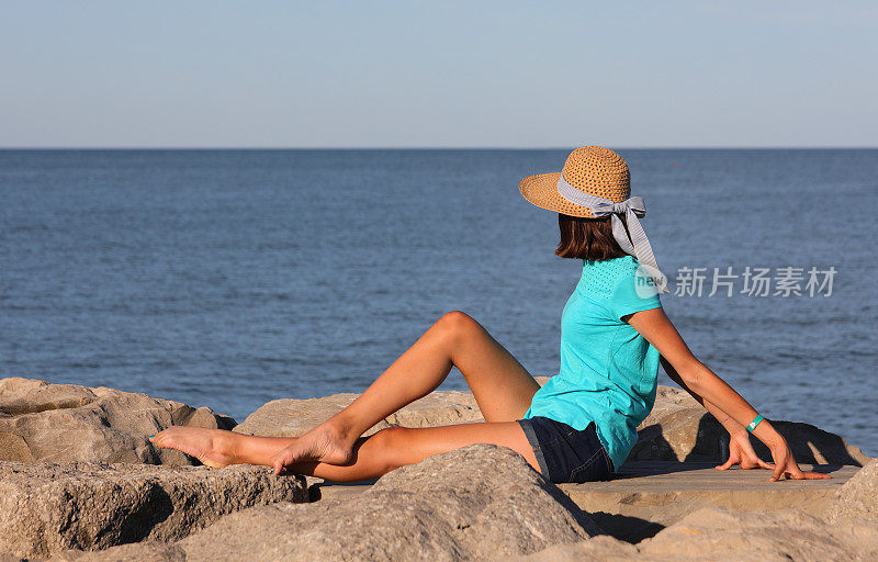 戴草帽的女孩在海边的岩石上