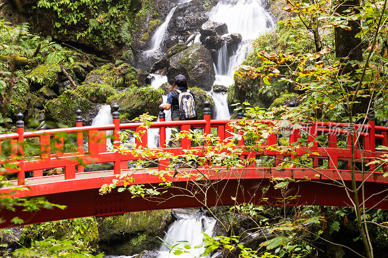 日本的女性游客在一座有瀑布的红色桥上驻足欣赏风景