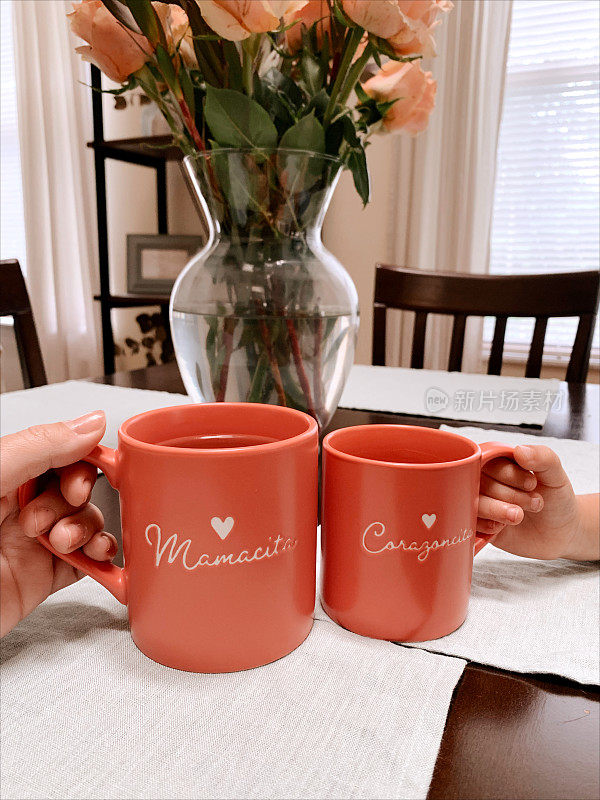 一对母女的手拿着粉色马克杯，上面写着“Mamacita”和“Corazoncita”，还有一颗心，西班牙语意思是可爱的“妈妈”和“小爱”，在2022年的秋天一起喝下午茶