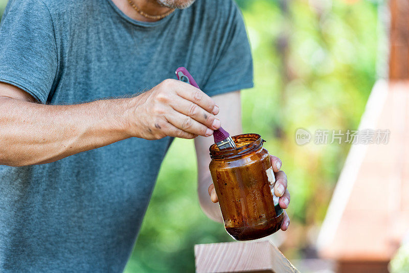 在阳光明媚的日子里，男人正在为家里的露台粉刷木板