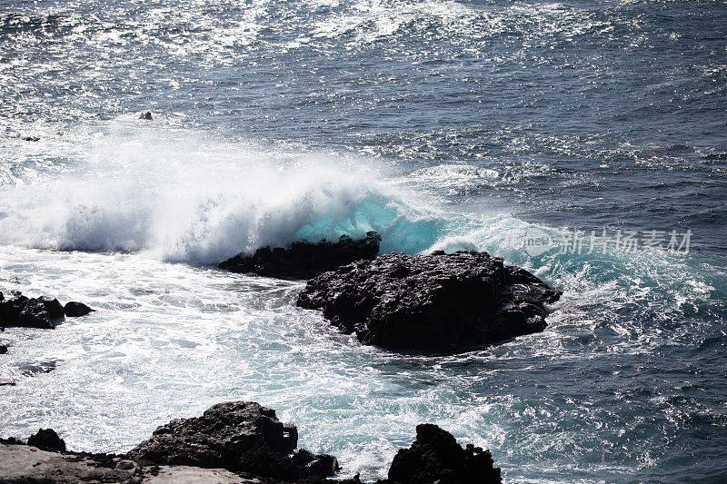 阳光照在海面上，海浪拍打着海面上的岩石的航拍照片