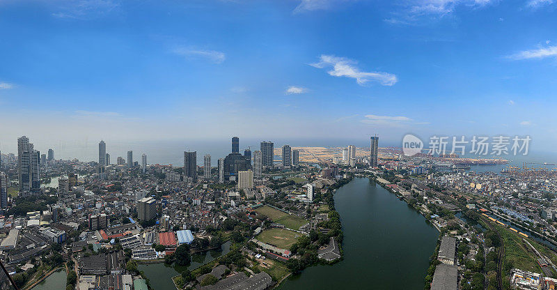 斯里兰卡科伦坡的城市景观图片，首都的摩天大楼，港口，道路，铁路轨道，港口起重机，蓝色多云的天空，重点在前景