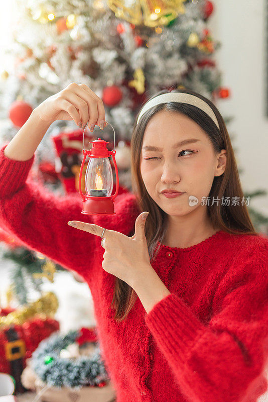 年轻美丽友好的亚洲女性女士，红色长袖毛衣衬衫和可爱的发带摆出不同的样子，在房间里装饰得很漂亮的圣诞树