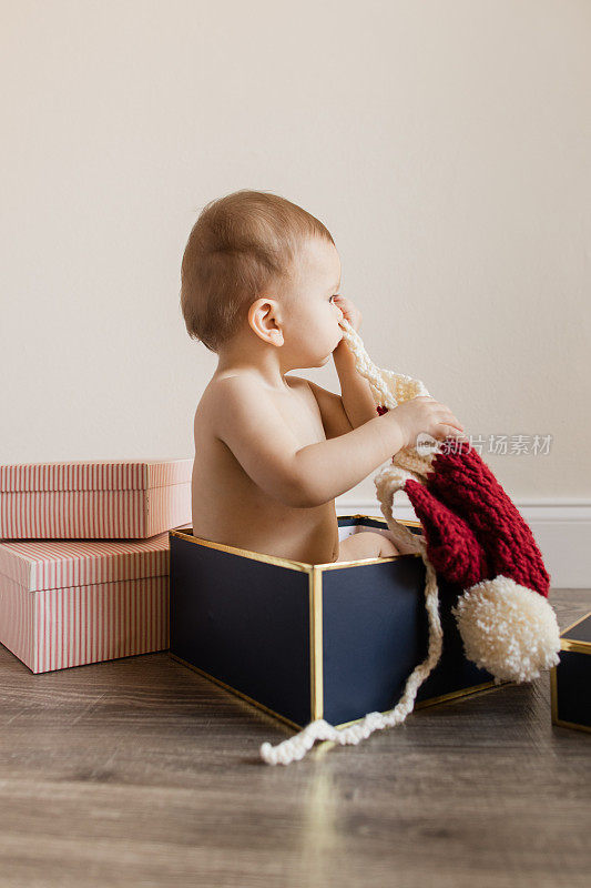 一个11个月大的圣诞男婴，有12只脚趾，穿着可持续的圣诞布尿布，坐在木地板上玩圣诞礼物，为他的生日和2022年的假期做准备
