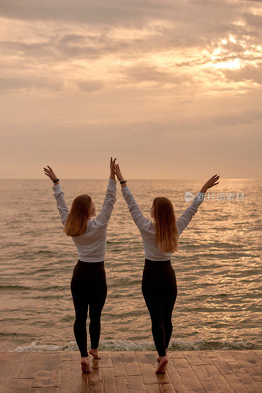健康的开始遇见日出——两姐妹双胞胎女孩穿着相同的衣服在海边。一对跳舞的夫妇和一对女双胞胎早上在海滩上训练。