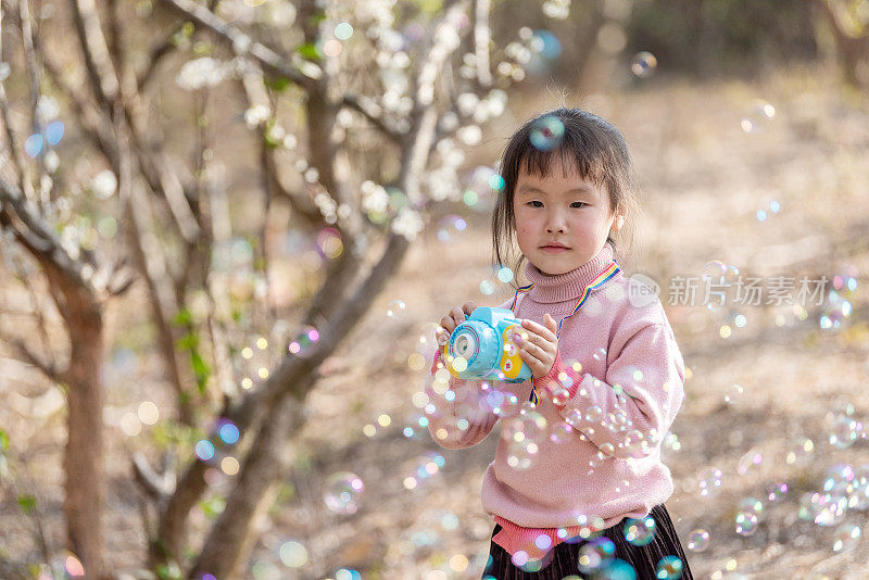 一个小女孩在梅园里玩泡泡机