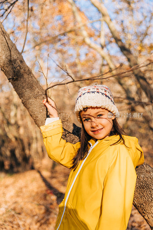 穿着黄色雨衣的开朗小女孩在美丽的秋林中摆姿势