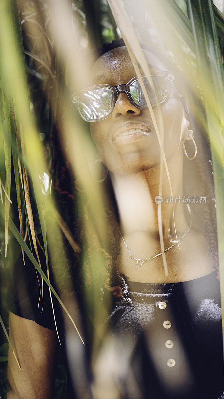 一个戴着墨镜的黑人妇女在热带棕榈树下的肖像