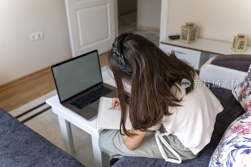 女孩用笔记本电脑学习。女孩在听在线教育课程。白皮肤的女孩在做笔记。