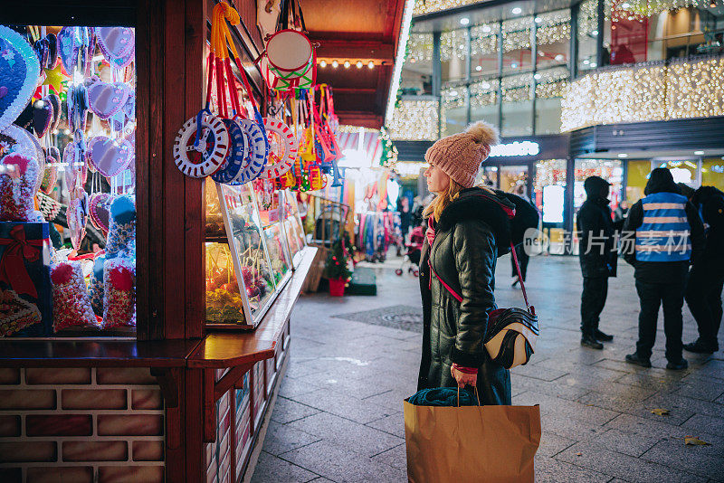 穿着保暖衣服的妇女站在圣诞街市场前，手里拿着糖果