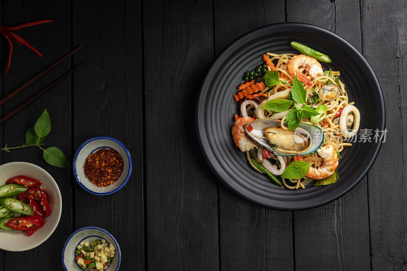 海鲜醉意面配虾鱿鱼蛤蜊辣椒和罗勒。泰国菜。黑色背景的桌子上，盘子里装着健康的亚洲人。前视图。