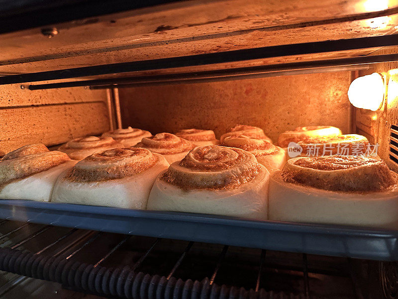 一排未煮熟的，自制的，肉桂漩涡丹麦糕点在热炉内的不粘锅烤盘上烘烤，五香面包在烘烤时上升，重点在前景