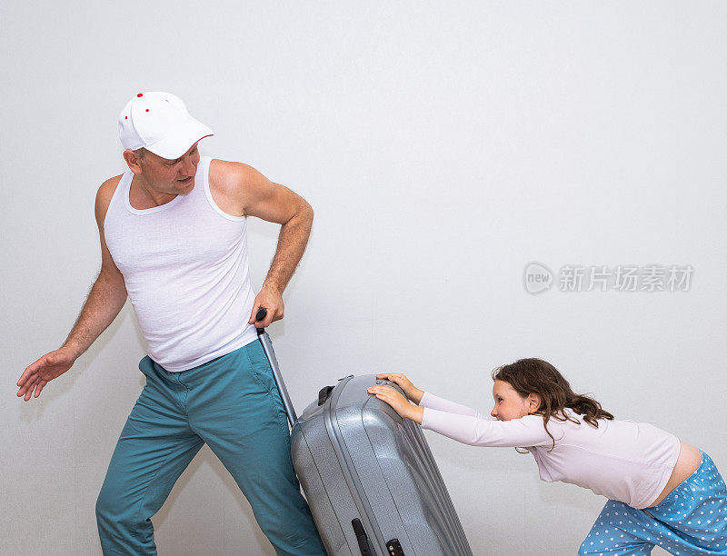 一名身穿白色t恤、头戴棒球帽的男子微笑着拖着一个手提箱。一个小女孩帮忙推箱子。为旅行收拾行李。