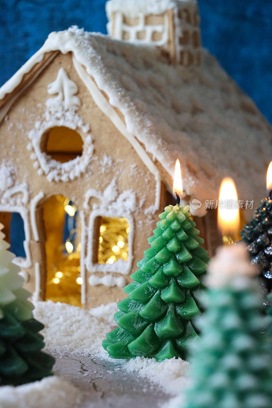 全帧图像的圣诞冷杉树森林场景，组点燃的圣诞树蜡烛姜饼屋，人造雪，斑驳的蓝色背景，重点在前景