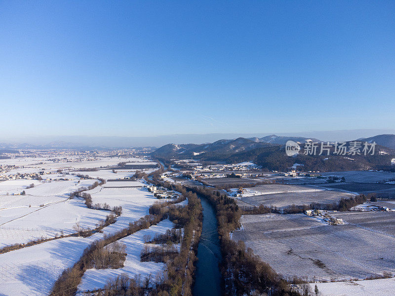 冬季航拍，一条河流在清澈的蓝天下蜿蜒穿过雪景和远处的群山。