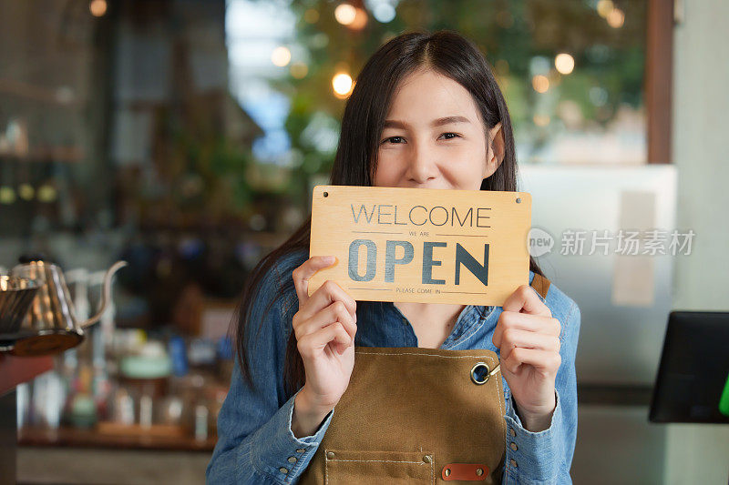 咖啡馆的老板漂亮的女商人一个亚洲的咖啡师员工拍照片来宣传商店，牌子上写着欢迎和开放咖啡馆和面包店她是一个小的家族企业