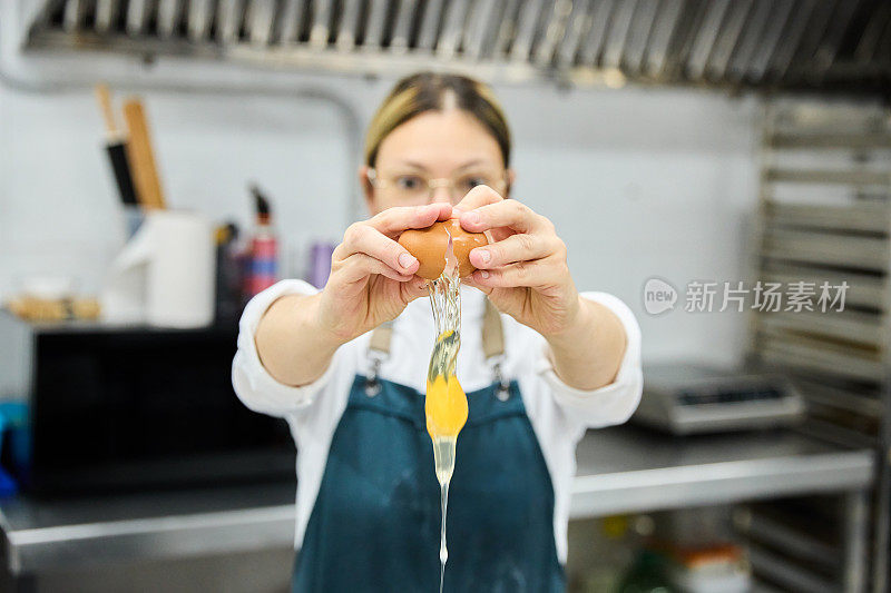 在面包房和蛋糕店的厨房里，年轻的女子在围裙上做饭，一边准备面团，一边把鸡蛋打进碗里