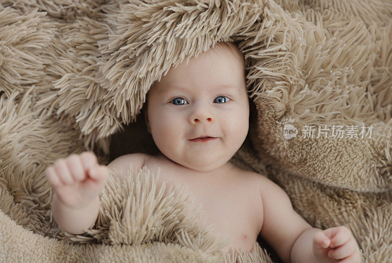 开心微笑的女婴躺在米色格子布上，看着镜头