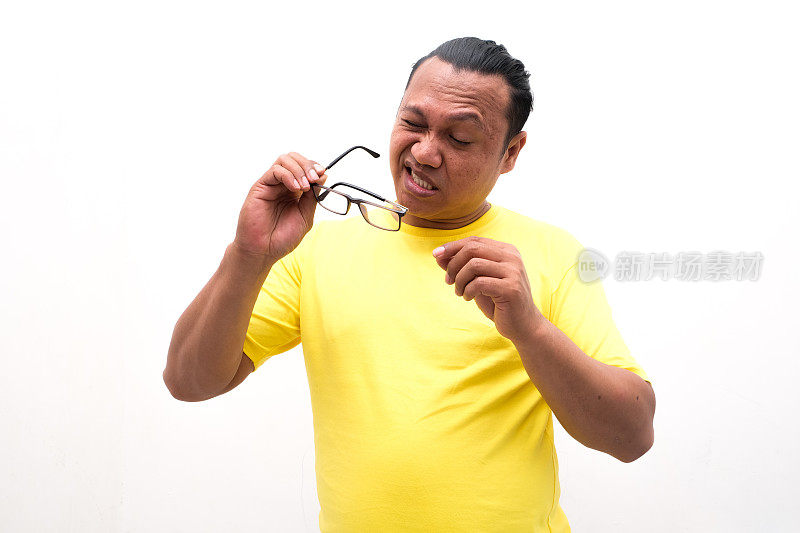 一名穿着黄色衬衫的亚洲男子的画像，因为他的眼睛有问题而戴着眼镜