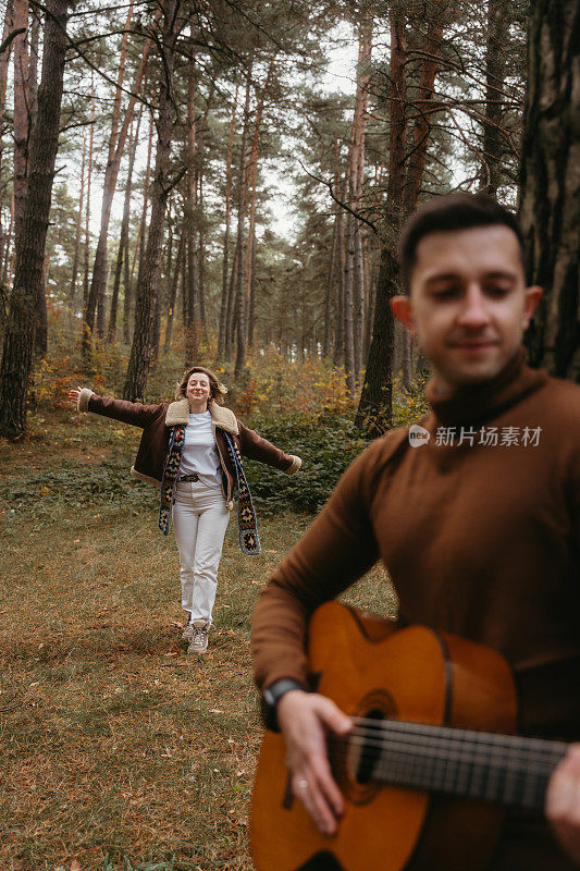 男人在树林里弹吉他，女人在秋天的公园里跟着他跳舞