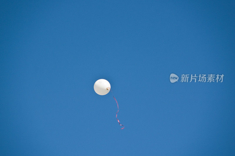 蓝色天空中系着红丝带的白色气球