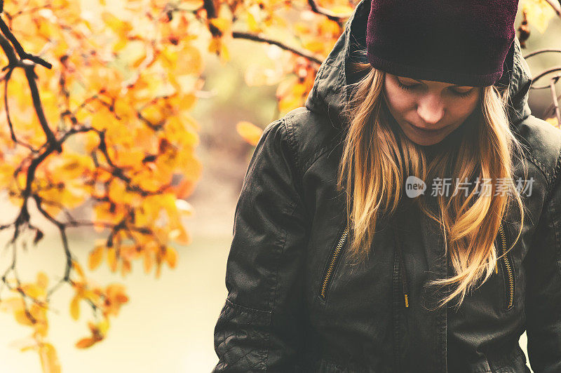 悲伤的女人在公园里散步，背景是秋叶