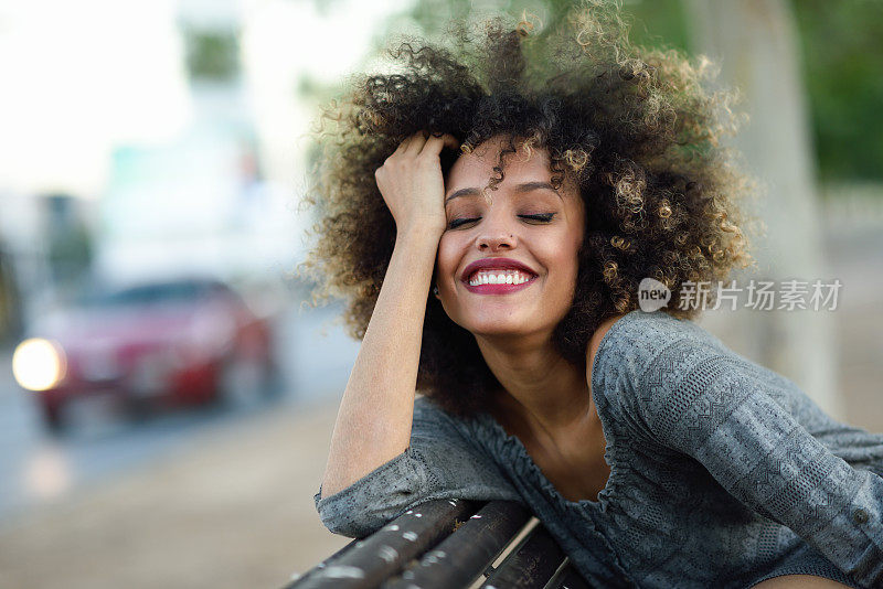 年轻的黑人妇女与非洲发型微笑在城市背景