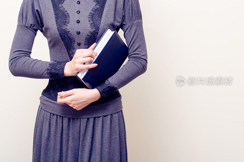 年轻漂亮的女人穿着灰色的复古衣服，拿着圣经