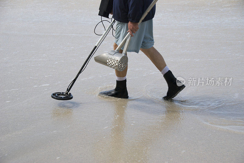 带着金属探测器的人在空旷的海滩上行走