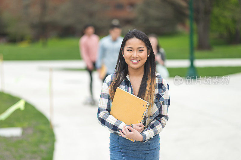 一名亚洲大学生带着笔记本和一个大大的微笑走向下一节课