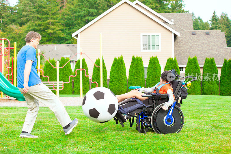 父亲和坐轮椅的残疾儿子在公园里踢足球