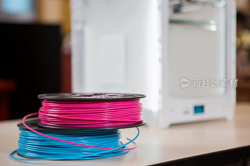 彩色的灯丝卷坐在书桌附近的3D打印机